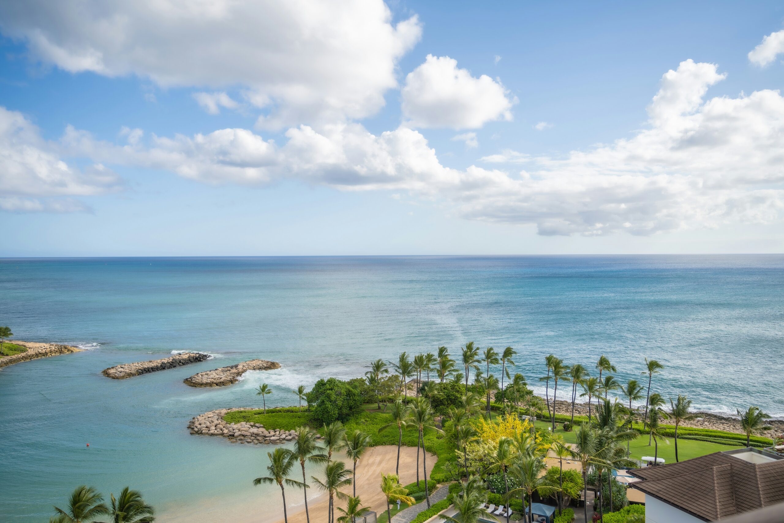 Birds eye view of a beach inlet in Hawaii. Blue ocean water with clouds in sky. Palm tree line the shore